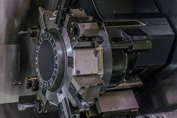 a complex industrial machine featuring multiple large, circular metal components with numerous bolts and gears. The machine parts are predominantly black and gray, with some silver accents