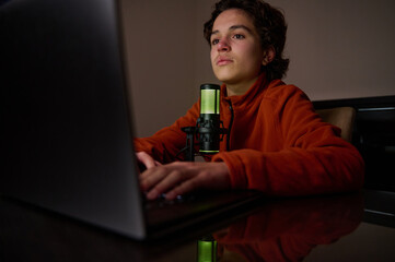 Young Person at Laptop With Microphone in Dim Room, Ready for Streaming or Recording