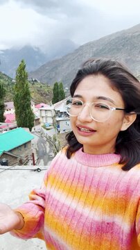 4K vertical selfie video of Indian woman vlogging while standing against mountains at Keylong, Himachal Pradesh, India. Travel blogger making content on location. Happy Indian travel blogger talking a