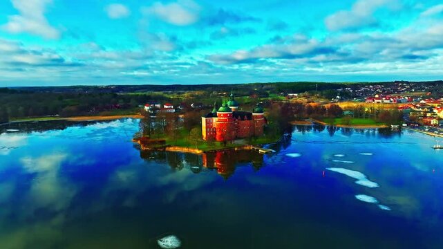 Aerial view of Gripsholm Castle, with its red brick walls mirrored in the dark blue water, creating a striking contrast against the cold sky, Mariefred, Sodermanland County, Sweden.