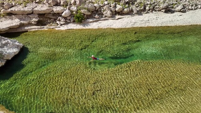 aerial view of woman floating on her back in the crystal clear turquoise and green water of Wadi Hadhbram in Oman. Enjoying relaxation and solitude in stunning natural desert oasis valley in Dhofar