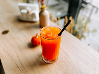 Bright orange drink with ice on wooden table near small orange and bottle