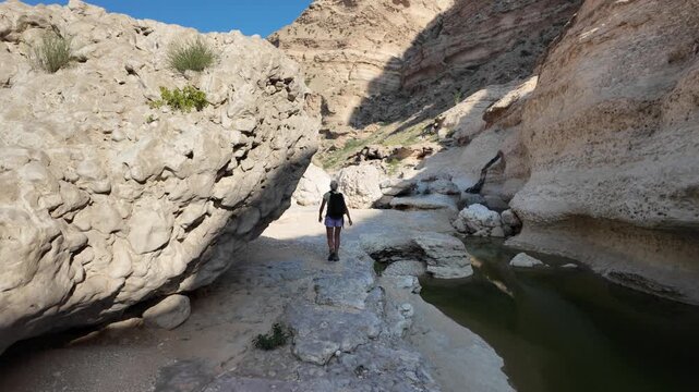 Woman backpacking, hiking through a rocky dry wadi in Wadi Hadhbram, Hasik, Oman, exploring the natural outdoor environment and enjoying adventure travel in Dhofar region