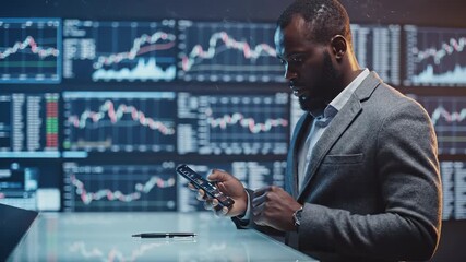 Businessman analyzes trading data on phone near charts. Trader checks market on smartphone by stock displays. Investor monitors trading trends. Man analyzes financial data with phone in office. - Powered by Adobe