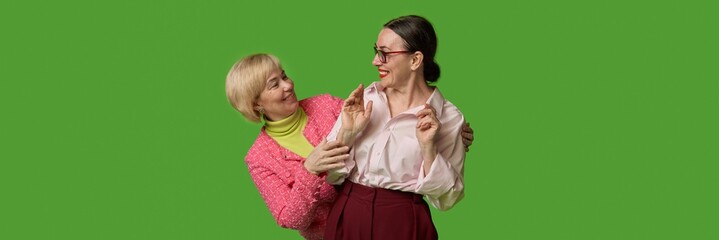 Senior women sharing playful moment on green backdrop. Concept of emotional wellness, friendship, lifestyle articles for 60 plus, healthcare communication and home wellness content. Banner