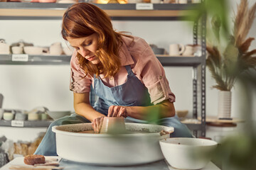 Focused Pottery Artist Shapes Clay on Wheel in Studio Workshop Wearing Apron