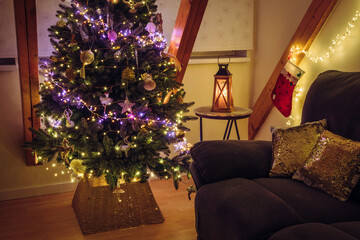 A basketweave Christmas tree collar with pink and yellow string lights illuminating the Christmas tree, decorated with fantasy-themed ornaments at home at night.