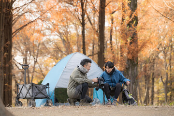 秋のキャンプ場で笑顔の男性2人がテント前楽しく話す休日のアウトドアキャンプシーン　カメラで何かを撮影する