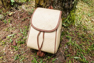 A backpack made of woven natural rattan in beige and brown colors placed on grass. Flatlay high top angle view.	