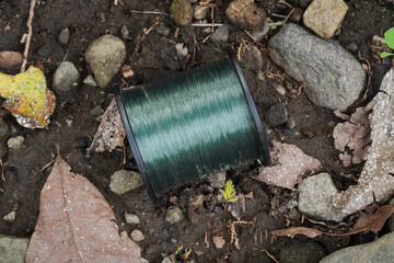 A spool of fishing line placed on the ground by the riverbank.