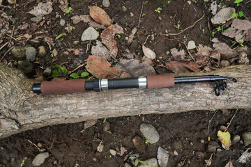 A fishing rod with a fishing reel placed on a wood tree trunk surface during fishing activities.