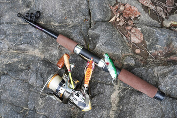 A fishing rod with a fishing reel placed on a rocky surface during fishing activities.