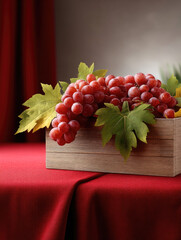 Naklejka premium Red grape cluster with green leaves in wooden box on red fabric, natural light, fresh and vibrant still life composition