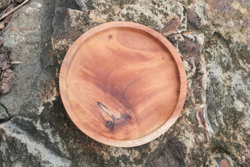 A wooden round plate placed on a rough stone surface. Flatlay high top angle view.
