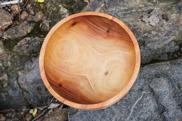 A wooden round bowl placed on a rough stone surface. Flatlay high top angle view.