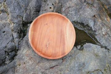 A wooden round plate placed on a rough stone surface. Flatlay high top angle view.