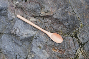 A wooden tablespoon placed on a rough stone surface. Flatlay high top angle view.