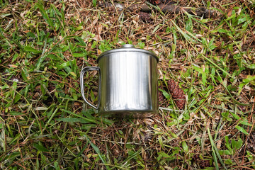 A silver-colored stainless steel mug placed on a grassy surface. Flatlay high top angle view.