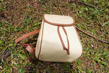 A backpack made of woven natural rattan in beige and brown colors placed on grass. Flatlay high top angle view.