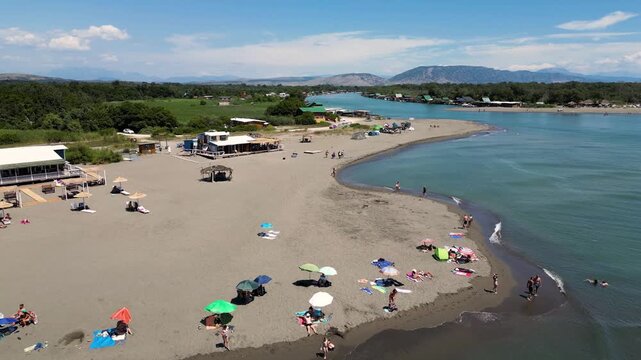 Aerial view of Velika Plaza's dark sandy beach meeting the turquoise waters, with people enjoying the sunny day, Velika Plaza, Ulcinj Municipality, Montenegro.