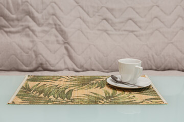 White coffee cup on a patterned placemat on a glass table