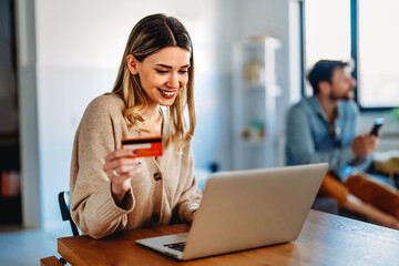 Smiling woman holding a credit card and shopping online at home with a laptop, online purchase