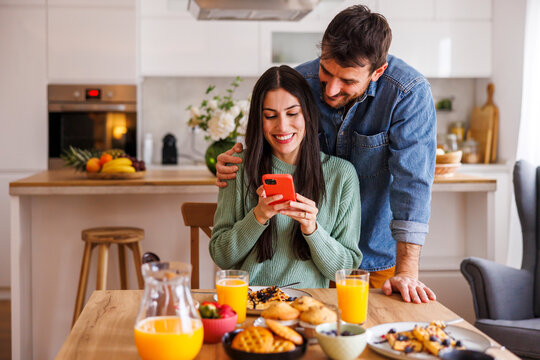Couple using smart phone while having breakfast at home