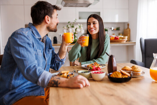 Couple drinking fresh orange juice while having breakfast at home