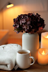 Cozy winter home interior with warm candlelight, wool sweater, hot tea and LED decor creating a calm hygge atmosphere
