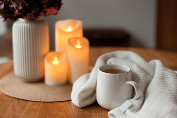 Cozy winter home interior with warm candlelight, wool sweater, hot tea and LED decor creating a calm hygge atmosphere