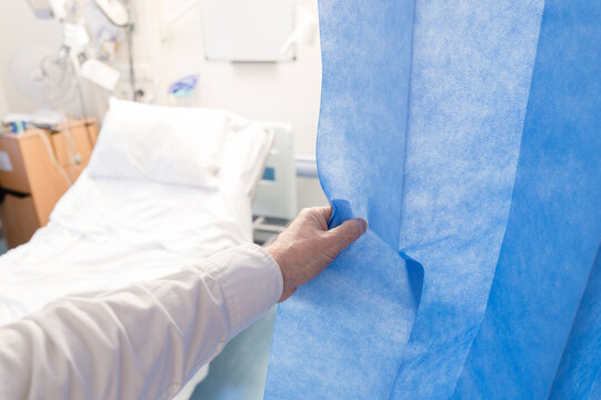 Hospital doctor seen pushing back blue privacy curtains within an accident and emergency room within a typical hospital. The patient has since been discharged.