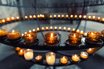Burning votive candles warm glow in circular stand rack at French catholic cathedral church dark background. Prayer, hope, faith, remembrance prayer spirit in tranquil atmosphere
