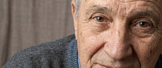 Elderly man's face showing wrinkles and lines around his eyes, representing the natural of aging and the experience of life in a close up portrait