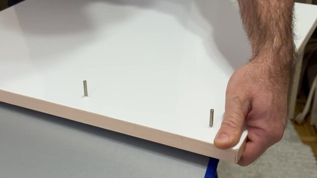 Installing upper board of shelf with wooden dowel pins in apartment closeup. Man assembles furniture carcass of plywood details working at home. High quality 4k footage