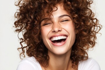 Joyful woman with curly hair smiling broadly, showcasing happiness, vitality, and confidence against a clean white background, expressing pure joy and positivity.