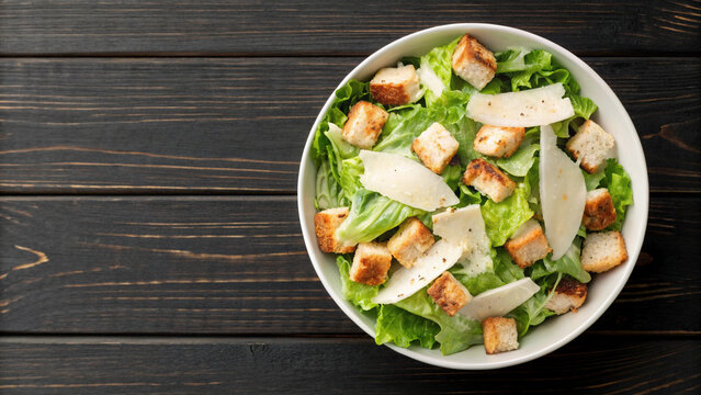 Caesar salad with romaine lettuce, chicken, croutons and parmesan on dark wooden background top view. Healthy food. Space for text - Powered by Adobe