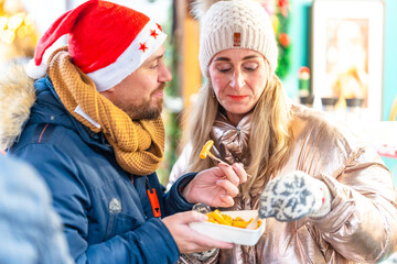 Happy couple enjoying a warm meal at a Bavarian Christmas market in Germany surrounded by festive winter lights