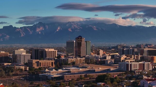 Aerial view of Tucson's skyline with buildings contrasting against the backdrop of majestic mountains and soft clouds, Tucson, Arizona, United States.