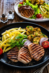 Grilled pork tenderloin steaks with baked potatoes and boiled yellow beans on wooden table
