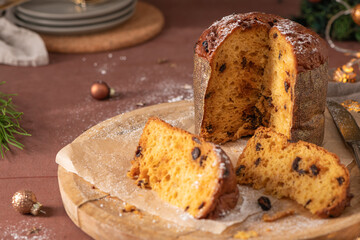A delectable Panettone with raisins and a dusting of powdered sugar, presented sliced on a rustic wooden board amidst a festive, warm-toned holiday table setting