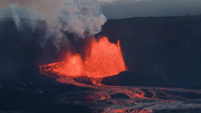 Aerial view of lava spewing from a volcano, contrasting the bright molten rock with the dark, hardened landscape and plumes of smoke, Kilauea, Hawaii, United States.