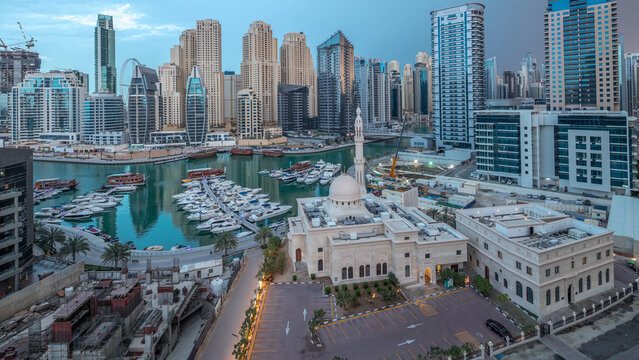 Yachts in Dubai Marina flanked by the Al Rahim Mosque and residential towers and skyscrapers aerial night to day timelapse.