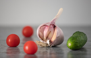 Garlic head surrounded by cherry tomatoes and cucumber