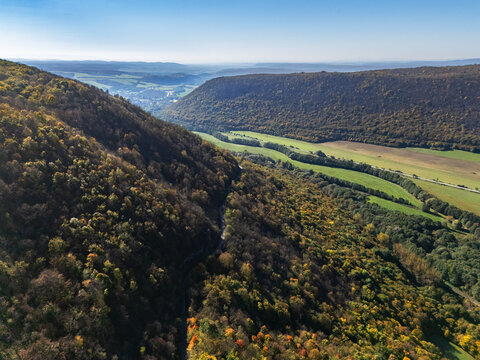 Aerial view of rolling hills and lush forests in vibrant autumnal hues, where shadows dance on the landscape, Plesivec, Kosice Region, Slovakia.