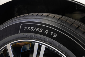 Close-up detail shot of a 235/55 R19 car tire sidewall and alloy wheel. Brand new tire, low angle, no people
