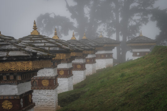 View of the Dochula Chorten's 108 memorial stupas stand in solemn rows, their white bases and grey roofs contrasting with the green hill, Hungtso, Bhutan.