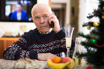 Lonely elderly pensioner wishes Merry Christmas by phone to friends and acquaintances sitting at...