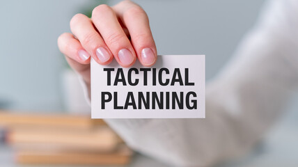 A person is holding a white card that says Tactical Planning