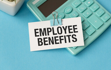 A calculator sits on a blue surface with a white sign that says Employee Benefits.