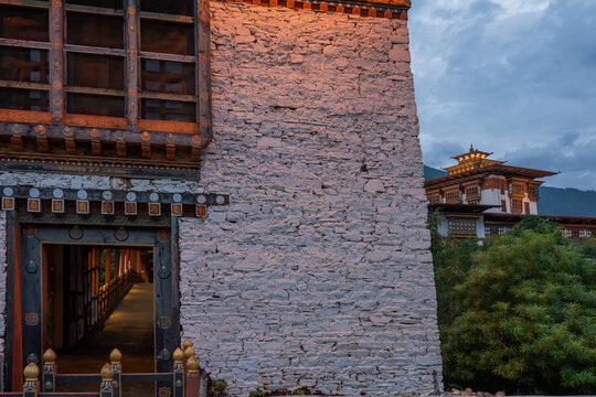 View of warm light spilling from an open doorway contrasts against the cool, rough texture of a whitewashed stone wall, Punakha, Bhutan.